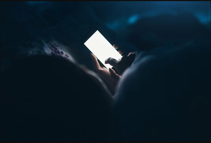 Person lying in bed in the dark using cell phone