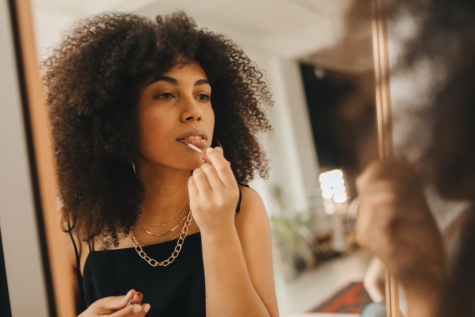Young woman applying makeup in the mirror