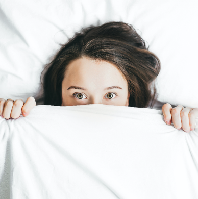 Jeune femme allongée dans son lit et partiellement couverte de couvertures Jeune femme allongée dans son lit et partiellement couverte de couvertures